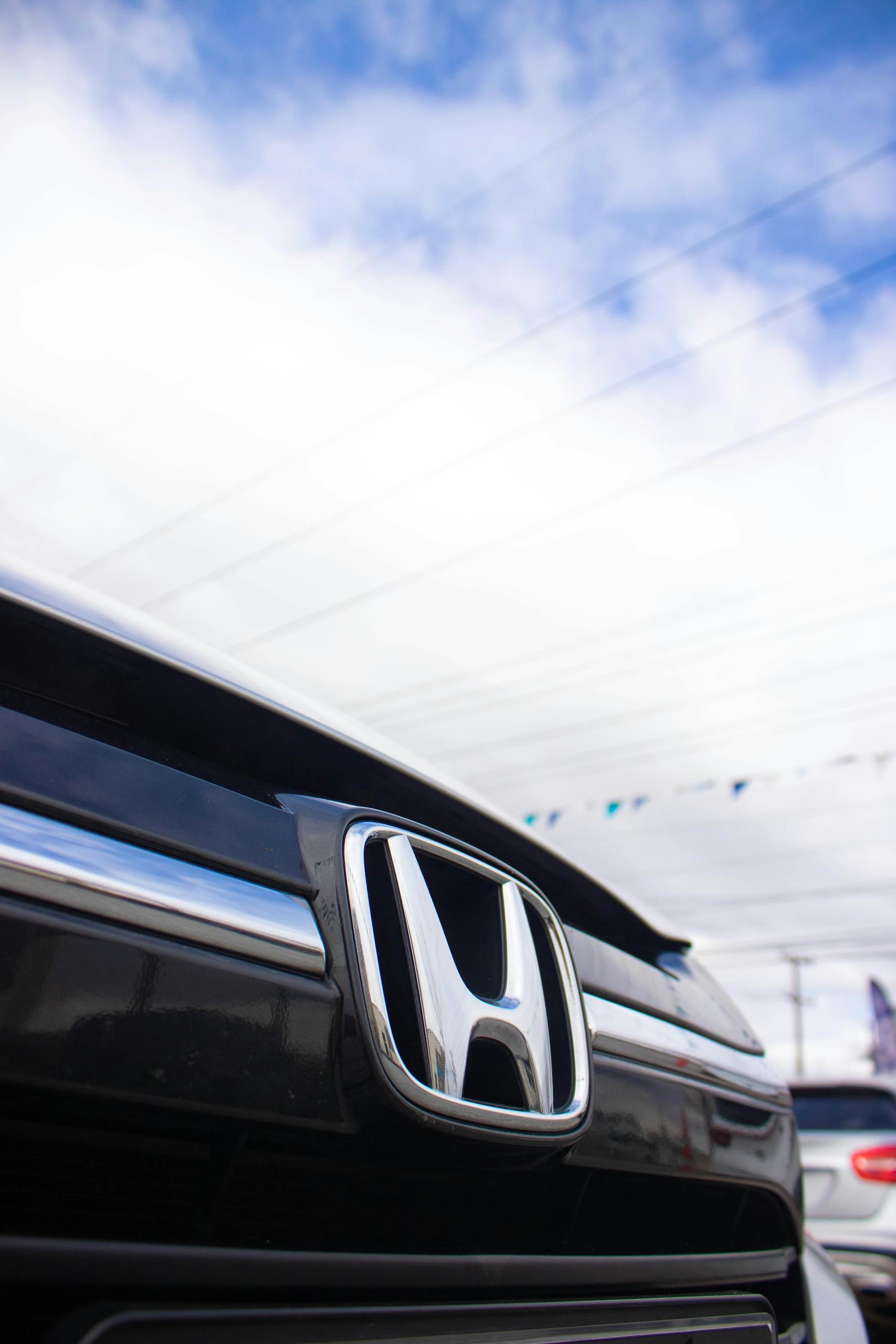 Detailed shot of a Honda car grille with sky background, showcasing automotive design.