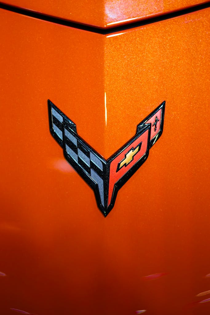 Detailed view of Chevrolet Corvette logo on a vibrant orange car hood, showcasing automotive design.
