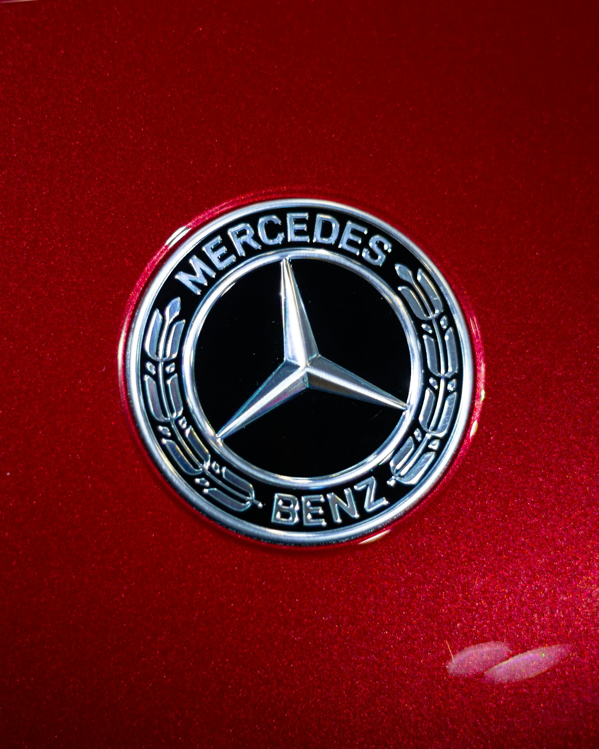 Detailed view of the Mercedes-Benz emblem on a sleek red car surface.